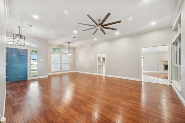 unfurnished living room with hardwood / wood-style floors, ceiling fan with notable chandelier, ornamental molding, a fireplace, and a textured ceiling