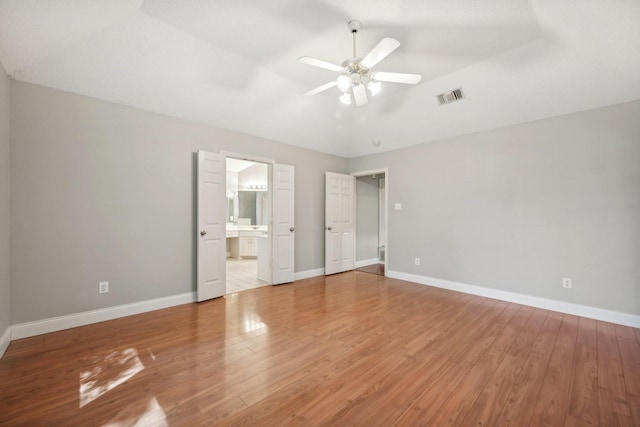 unfurnished bedroom with ceiling fan, ensuite bathroom, vaulted ceiling, and hardwood / wood-style flooring