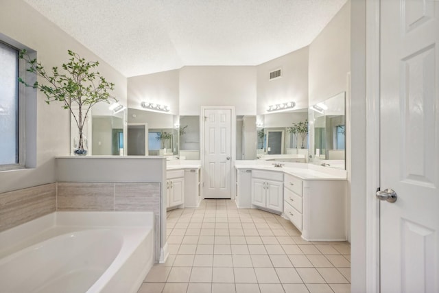 bathroom with vanity, a textured ceiling, vaulted ceiling, tile patterned flooring, and a tub