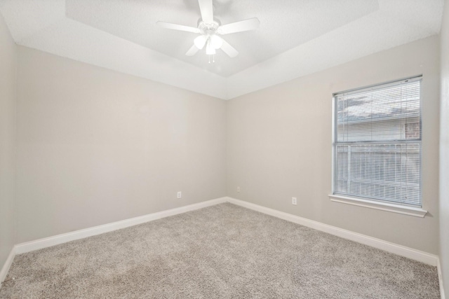 carpeted empty room with a tray ceiling, plenty of natural light, and ceiling fan