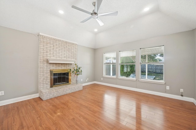 unfurnished living room featuring ceiling fan, a brick fireplace, light hardwood / wood-style flooring, a textured ceiling, and vaulted ceiling