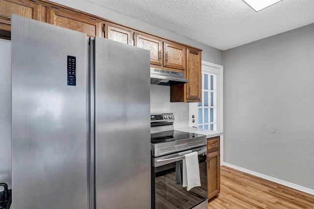 kitchen with appliances with stainless steel finishes, a textured ceiling, and light hardwood / wood-style flooring