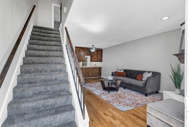 staircase featuring wood-type flooring, a textured ceiling, and ceiling fan