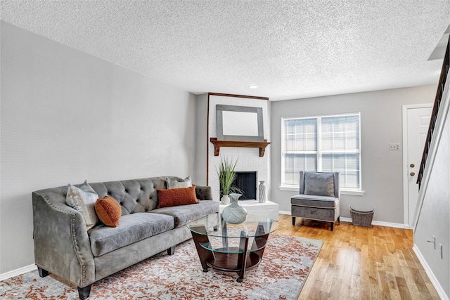 living room featuring a textured ceiling, light hardwood / wood-style floors, and a brick fireplace