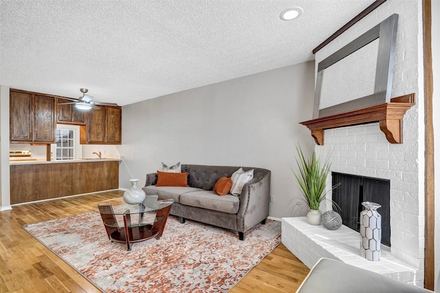 living room featuring light hardwood / wood-style flooring, ceiling fan, a textured ceiling, and a fireplace