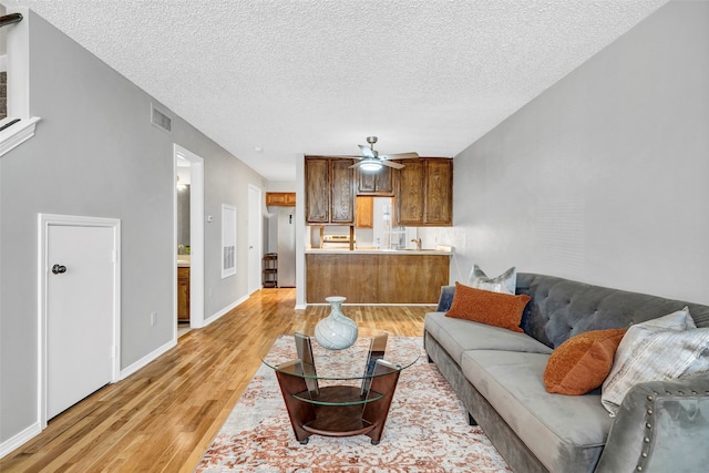 living room featuring light hardwood / wood-style floors, ceiling fan, and a textured ceiling