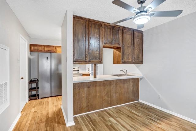 kitchen with stainless steel appliances, a textured ceiling, light hardwood / wood-style flooring, ceiling fan, and sink