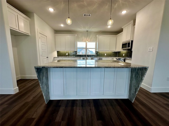 kitchen featuring white cabinetry, pendant lighting, stainless steel appliances, and dark stone counters