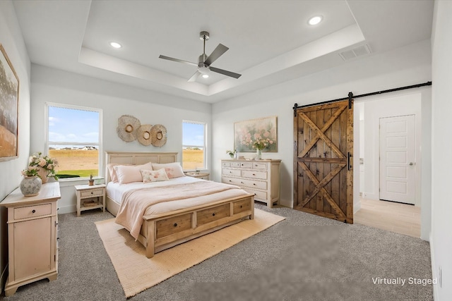 carpeted bedroom with a tray ceiling, a barn door, and ceiling fan