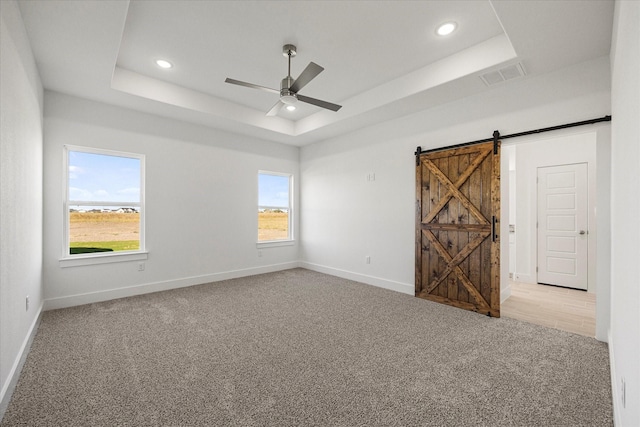 carpeted empty room with a tray ceiling, a barn door, and ceiling fan