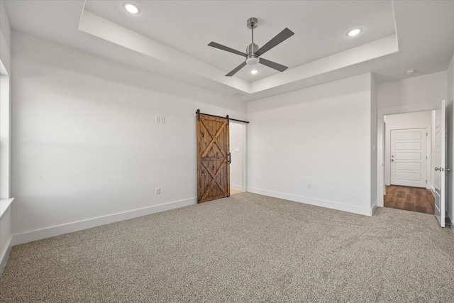 unfurnished bedroom with a barn door, carpet, ceiling fan, and a tray ceiling