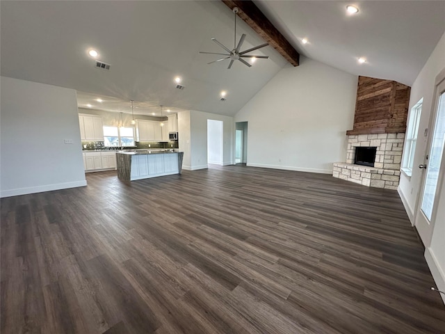 unfurnished living room with beamed ceiling, ceiling fan, a stone fireplace, and dark hardwood / wood-style flooring