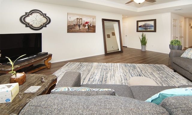 living room with ceiling fan, a tray ceiling, crown molding, and dark wood-type flooring