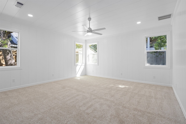 carpeted empty room with ceiling fan and wood walls