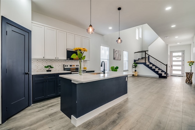 kitchen with pendant lighting, a kitchen island with sink, sink, white cabinets, and stainless steel appliances