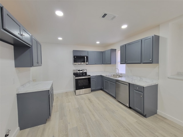 kitchen featuring stainless steel appliances, sink, light stone countertops, light hardwood / wood-style flooring, and gray cabinetry