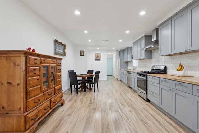 kitchen with gray cabinetry, light wood-type flooring, appliances with stainless steel finishes, and wall chimney exhaust hood