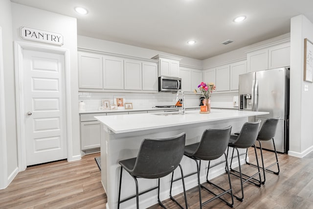 kitchen featuring appliances with stainless steel finishes, a kitchen breakfast bar, white cabinets, light hardwood / wood-style flooring, and a center island with sink