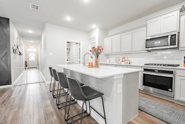 kitchen with light hardwood / wood-style flooring, a center island with sink, and appliances with stainless steel finishes