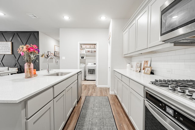 kitchen with sink, a center island with sink, hardwood / wood-style flooring, appliances with stainless steel finishes, and washer and dryer