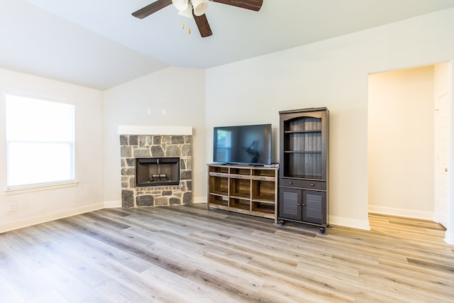 unfurnished living room featuring light hardwood / wood-style flooring, vaulted ceiling, ceiling fan, and a stone fireplace