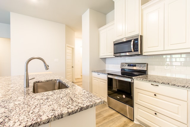 kitchen featuring appliances with stainless steel finishes, light hardwood / wood-style floors, white cabinets, light stone countertops, and sink