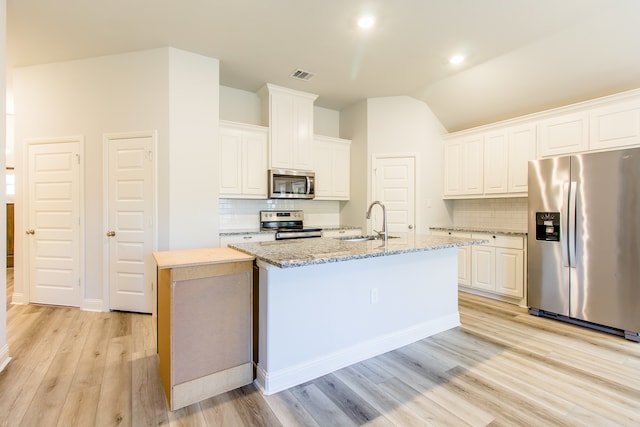 kitchen with white cabinetry, an island with sink, backsplash, stainless steel appliances, and light wood-type flooring