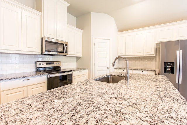 kitchen featuring light stone counters, sink, white cabinets, lofted ceiling, and appliances with stainless steel finishes