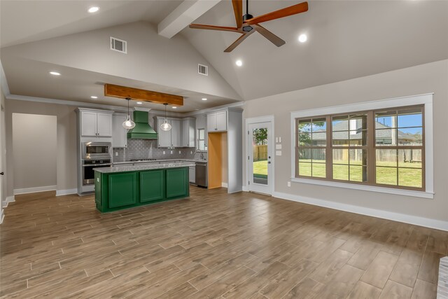 kitchen with hanging light fixtures, a kitchen island, wall chimney range hood, appliances with stainless steel finishes, and light wood-type flooring