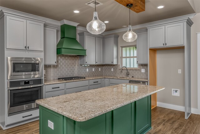 kitchen with appliances with stainless steel finishes, pendant lighting, a center island, custom exhaust hood, and hardwood / wood-style floors