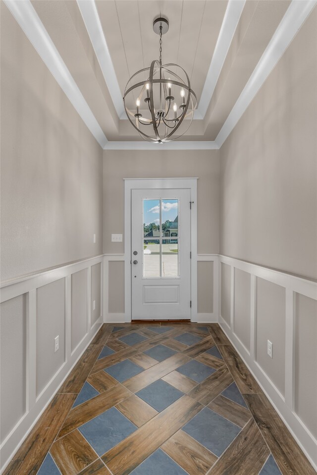 doorway to outside with a notable chandelier and a tray ceiling