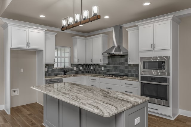 kitchen with a center island, wall chimney range hood, stainless steel appliances, and white cabinets