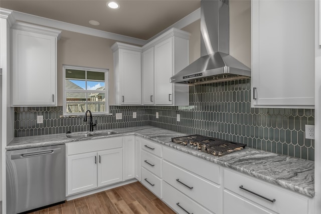 kitchen with appliances with stainless steel finishes, white cabinetry, and wall chimney range hood