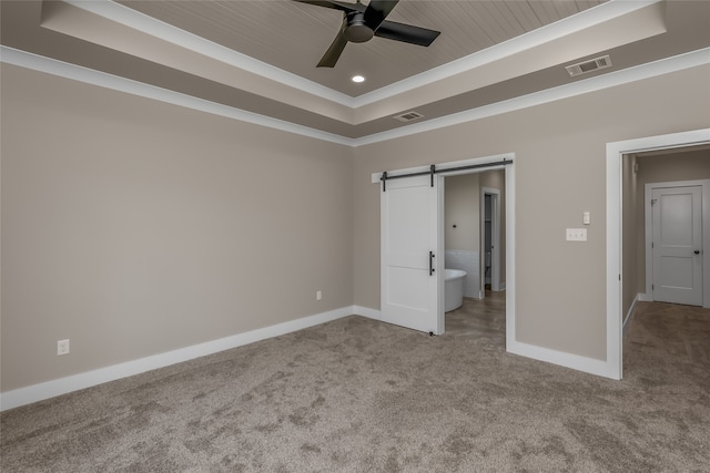 unfurnished bedroom featuring ceiling fan, ensuite bathroom, a raised ceiling, and a barn door