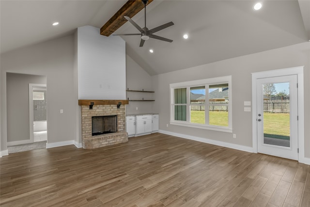 unfurnished living room featuring hardwood / wood-style flooring, beam ceiling, a fireplace, high vaulted ceiling, and ceiling fan