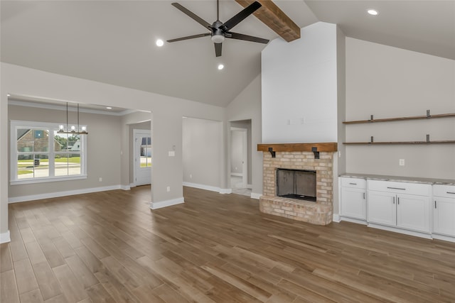 unfurnished living room with high vaulted ceiling, a brick fireplace, ceiling fan with notable chandelier, beam ceiling, and hardwood / wood-style floors