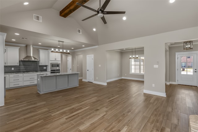 kitchen with wall chimney exhaust hood, a kitchen island with sink, plenty of natural light, and hardwood / wood-style flooring