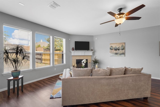 living room featuring ceiling fan, a tile fireplace, and dark wood-type flooring