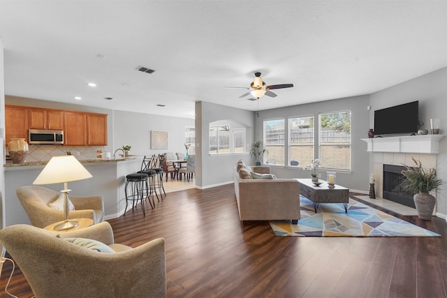 living room featuring a tile fireplace, dark hardwood / wood-style flooring, and ceiling fan