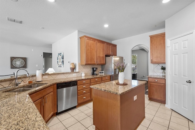 kitchen featuring light stone counters, a textured ceiling, sink, a kitchen island, and stainless steel appliances