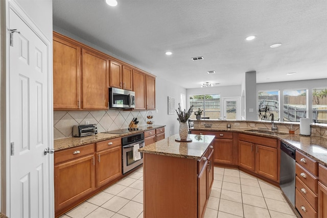 kitchen featuring light stone counters, light tile patterned floors, sink, appliances with stainless steel finishes, and a center island