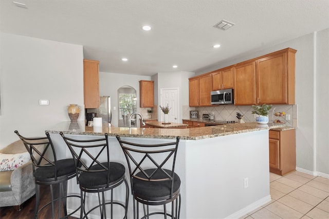 kitchen featuring appliances with stainless steel finishes, a breakfast bar area, kitchen peninsula, and light stone countertops