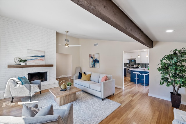 living room featuring vaulted ceiling with beams, ceiling fan, a fireplace, and light hardwood / wood-style floors