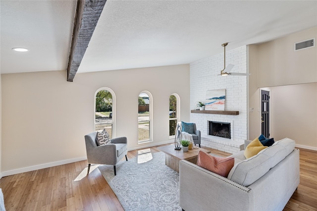 living room with lofted ceiling with beams, a brick fireplace, a textured ceiling, and light hardwood / wood-style floors