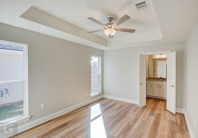 unfurnished bedroom featuring ceiling fan, light hardwood / wood-style flooring, a tray ceiling, and multiple windows