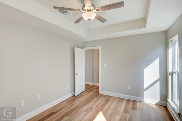 unfurnished room featuring ceiling fan, a tray ceiling, and light hardwood / wood-style flooring