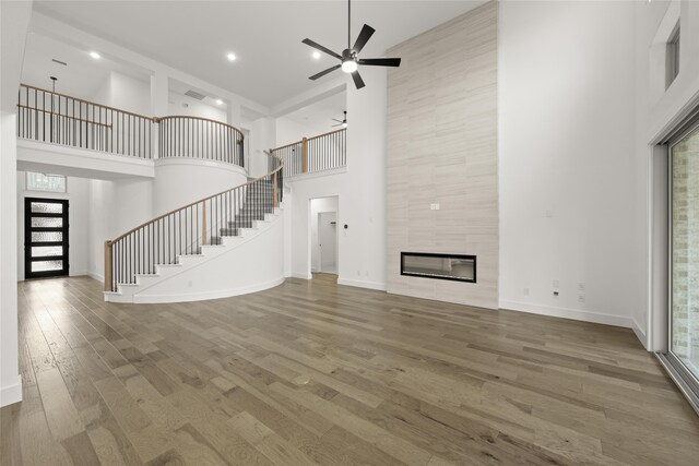 unfurnished living room with ceiling fan, wood-type flooring, a towering ceiling, and a fireplace