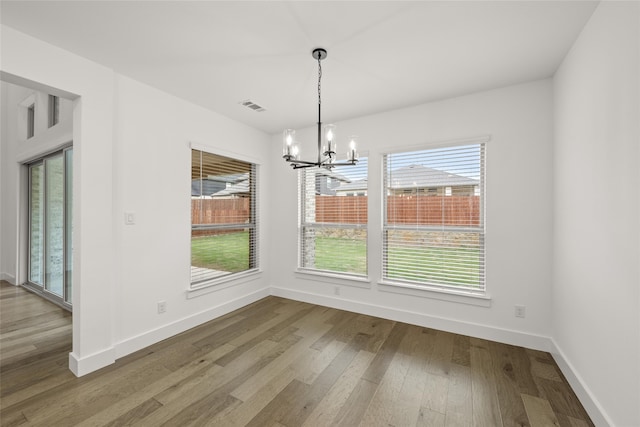 unfurnished dining area featuring a chandelier, plenty of natural light, and wood-type flooring