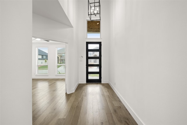 entryway with hardwood / wood-style floors, a towering ceiling, and an inviting chandelier