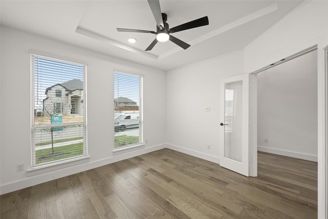 spare room with a raised ceiling, ceiling fan, and dark hardwood / wood-style flooring